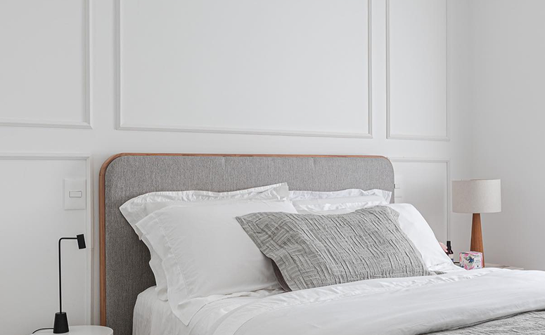 parede com boiserie atrás de uma cama com cabeceira cinza