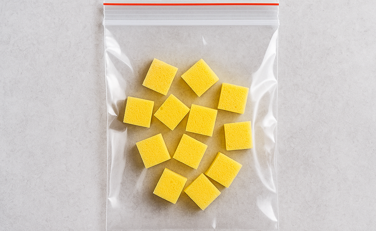 Saquinho plástico com pedaços de esponja amarela cortados em quadrados, pronto para ser congelado.