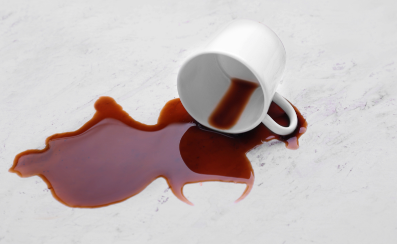 Xícara virada com café derramado sobre bancada com granito branco