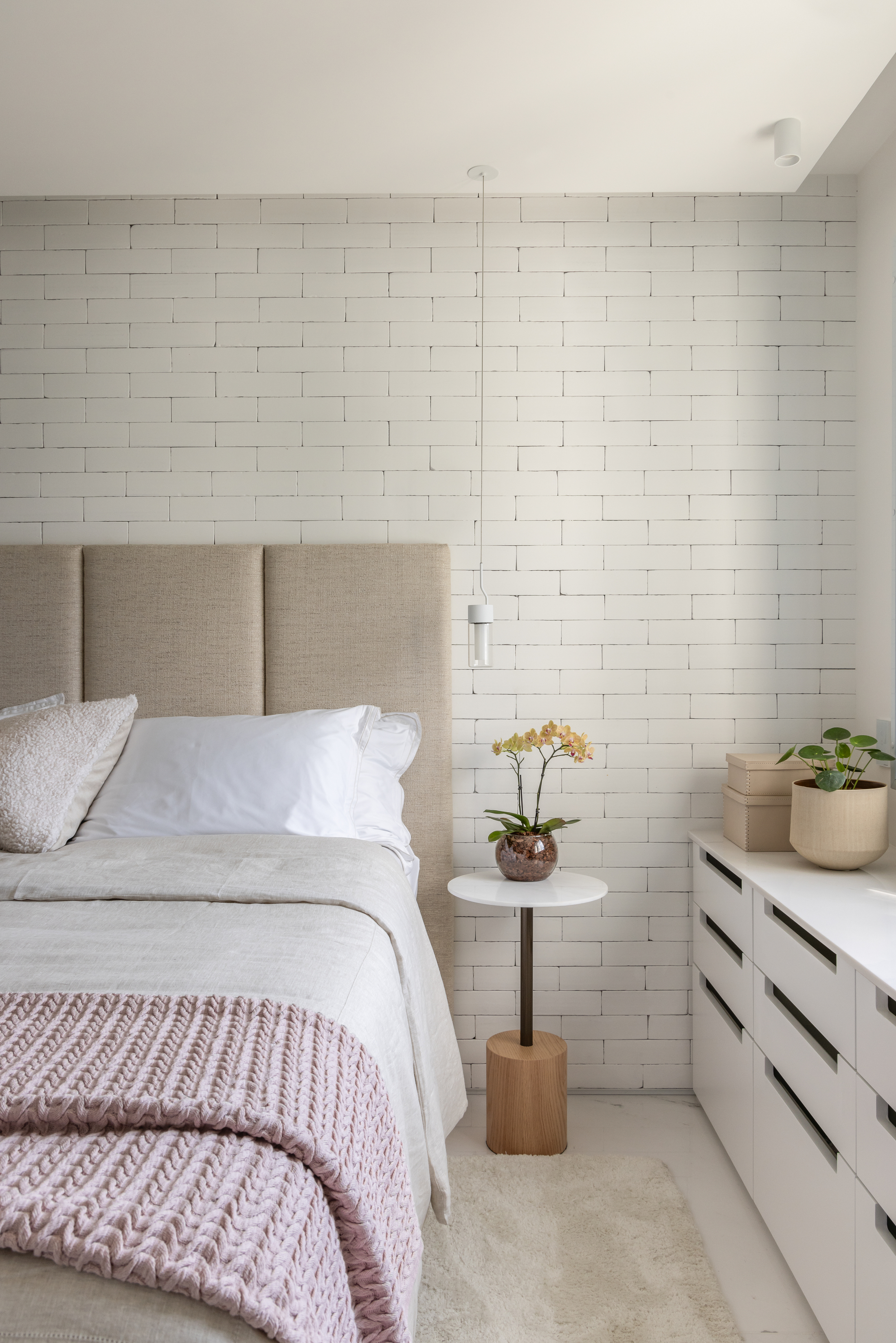 quarto branco com cabeceira estofada e pendente ao lado da cama.