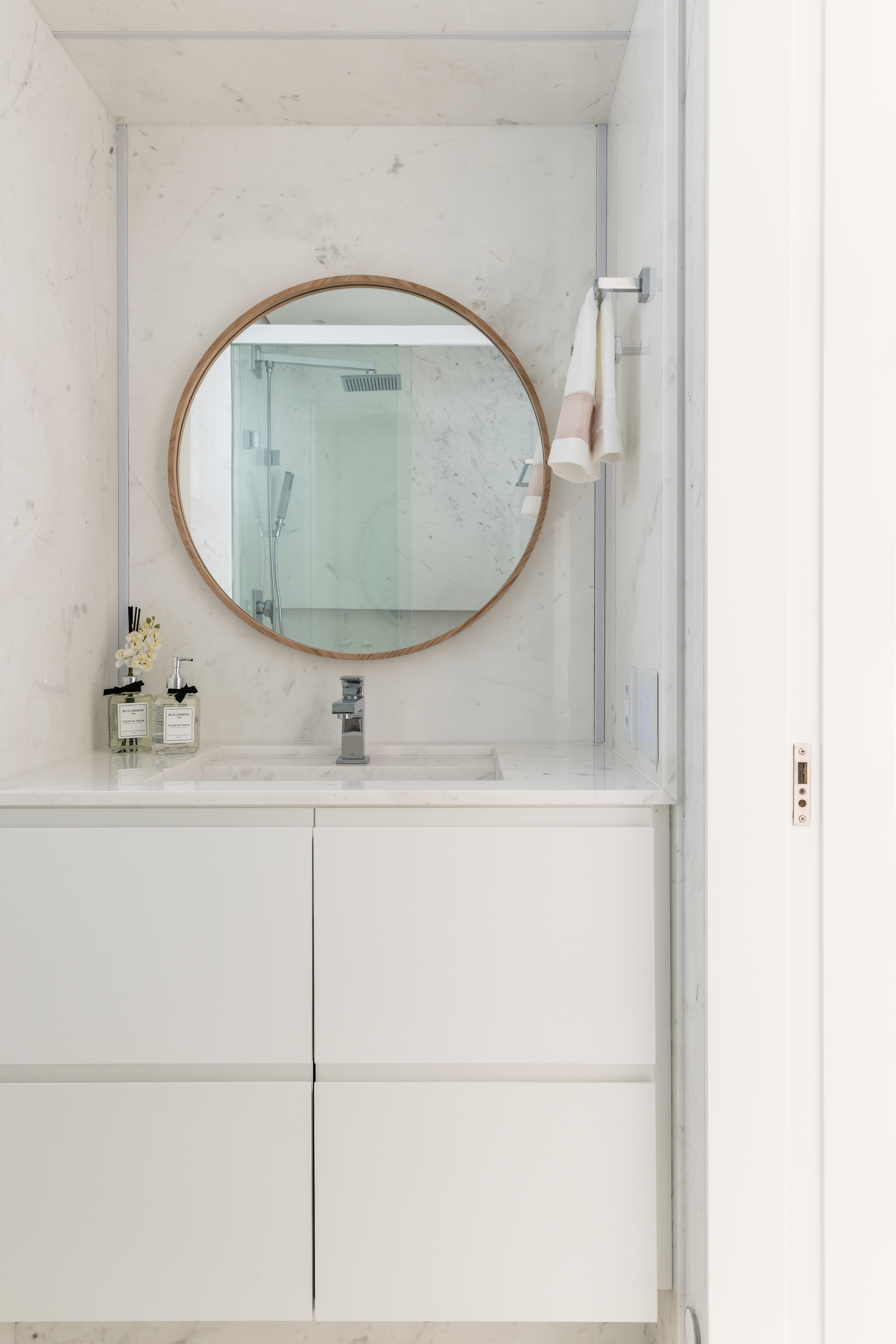 banheiro branco com mármore nas paredes e espelho redondo