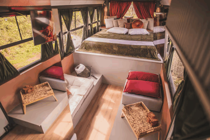 cama de casal posicionada ao fundo do ônibus casa, com vista para a natureza e decoração aconchegante