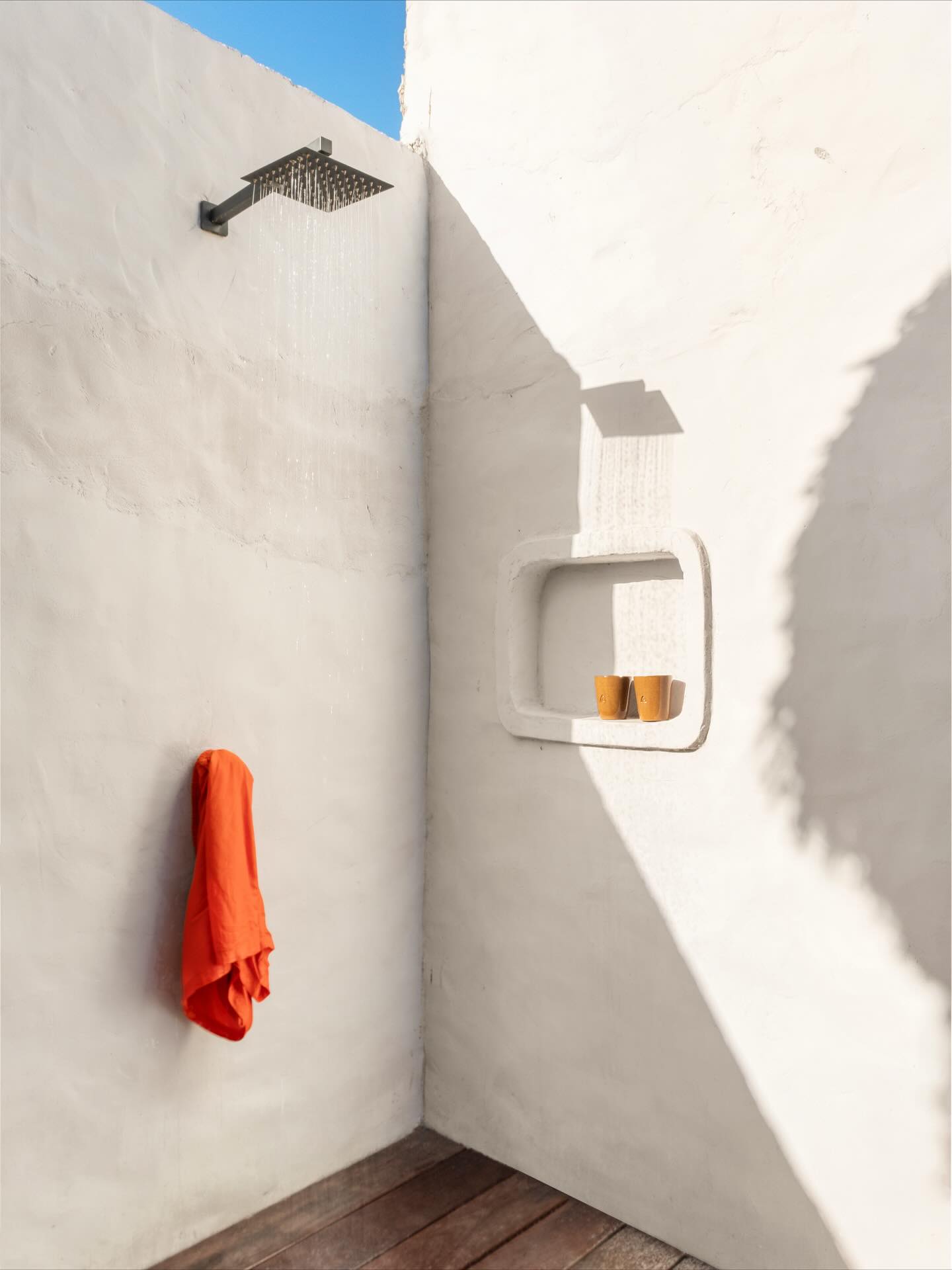 chuveirão no jardim com parede branca, piso de madeira e ducha moderna ao ar livre