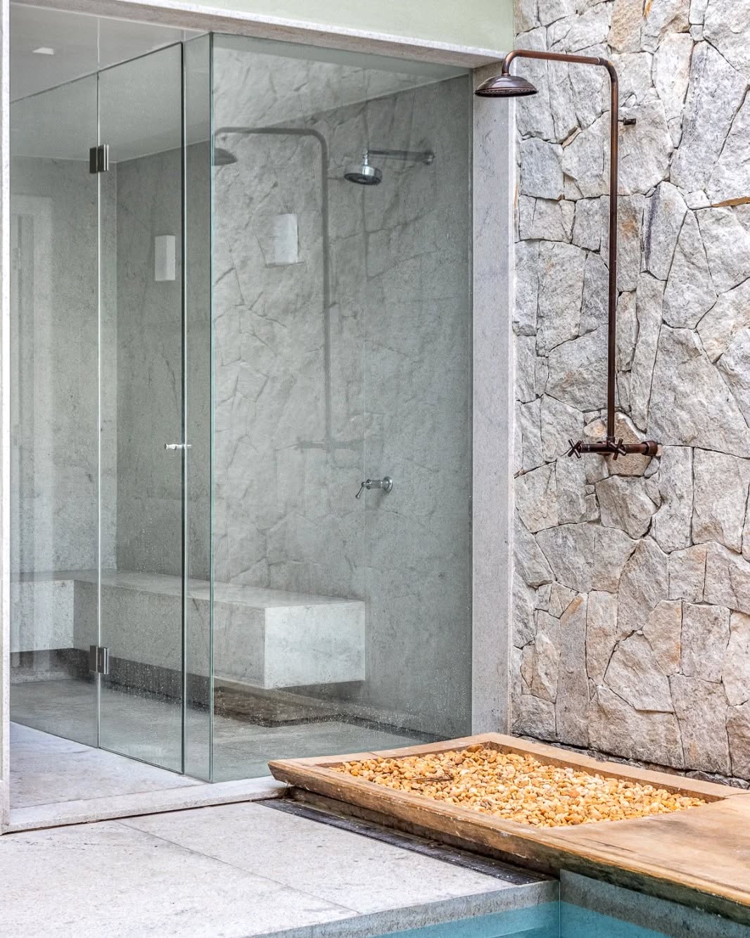 ducha externa em aço corten com estilo industrial e paredes de pedras naturais próximo à piscina.