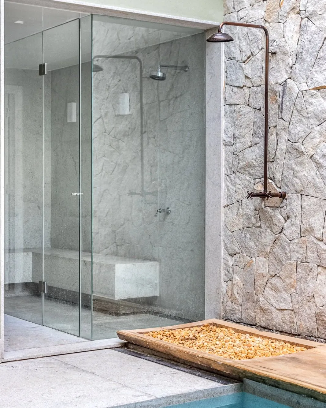 ducha externa em aço corten com estilo industrial e paredes de pedras naturais próximo à piscina.