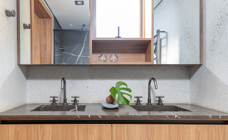 Banheiro de casal com bancada dupla, pedra natural clara e marcenaria em madeira.