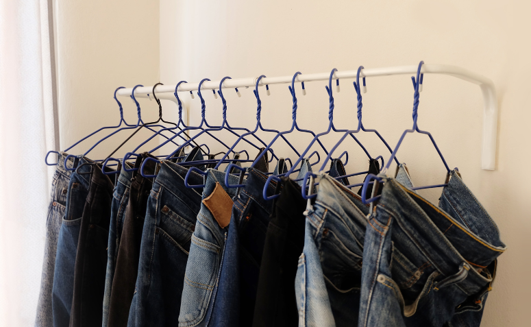 Calças jeans penduradas em uma arara com apoio de cabides.