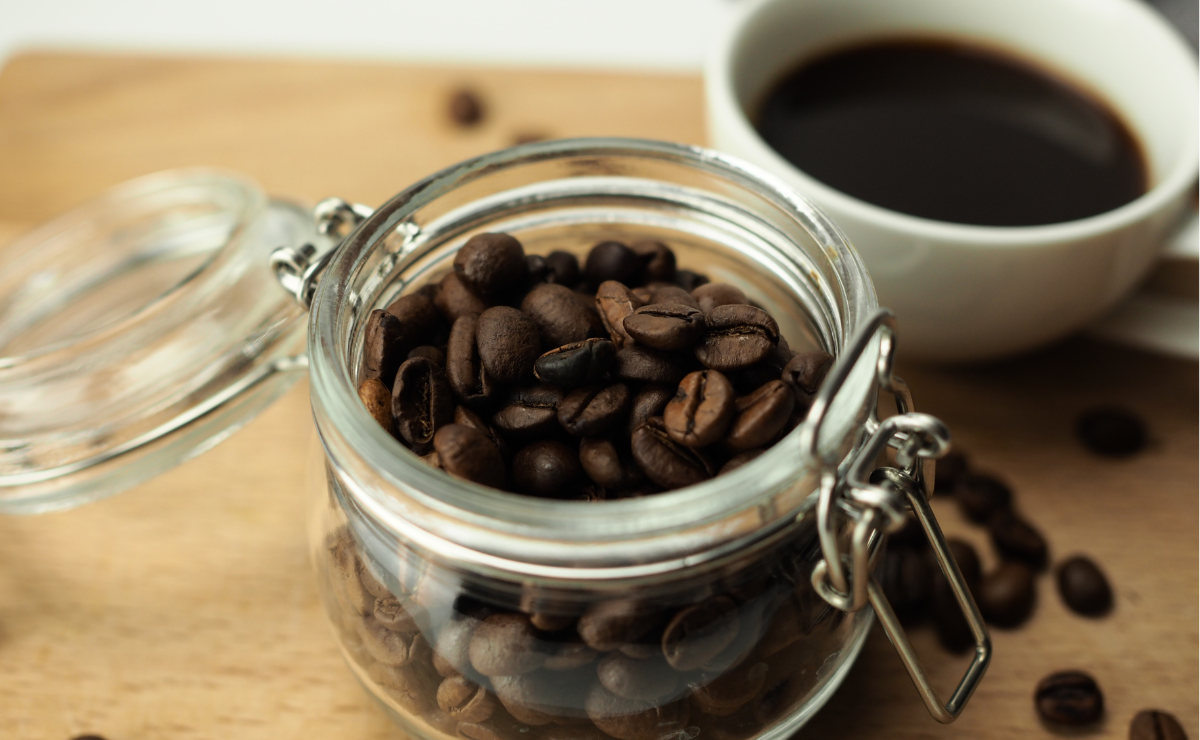 café em grãos armazenado em pote de vidro com tampa ao lado de xícara de café