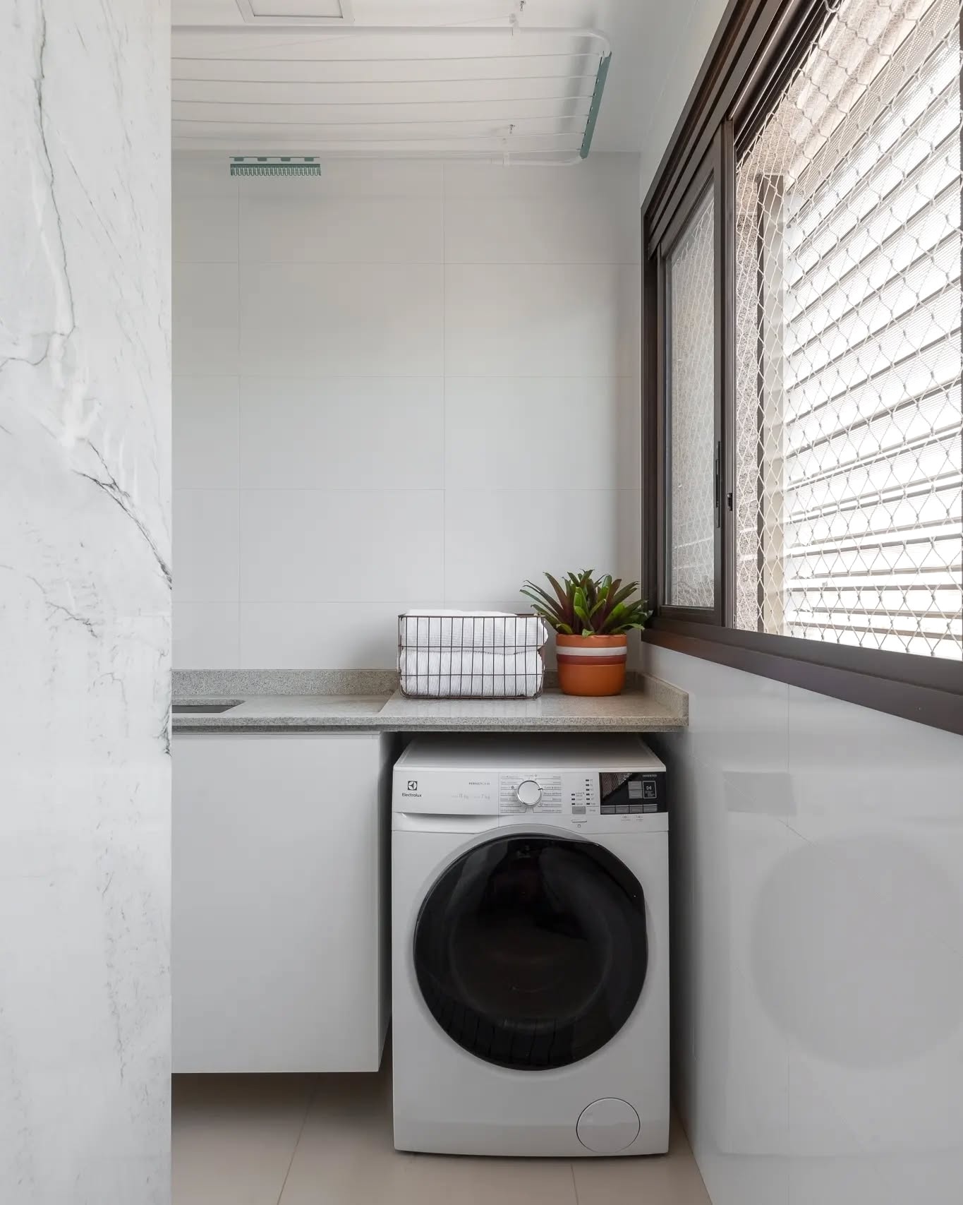 lavanderia branca pequena com máquina e bancada compacta