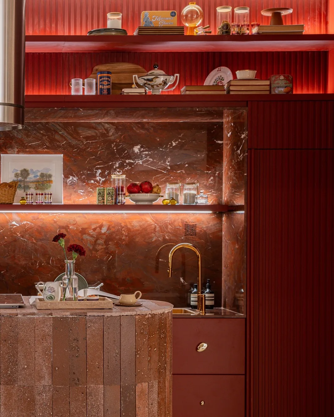 cozinha sofisticada com revestimento em mármore vermelho, iluminação quente e metais dourados.