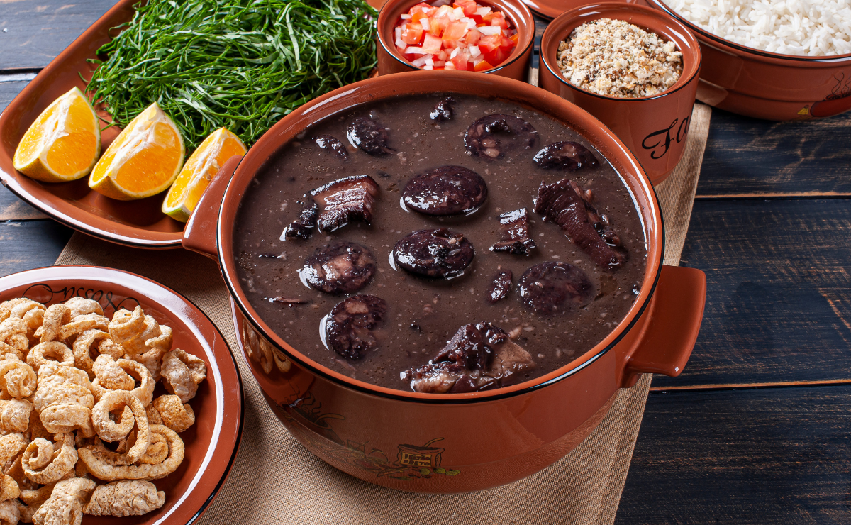feijoada brasileira servida com couve, arroz, farofa, laranja e torresmo em mesa tradicional