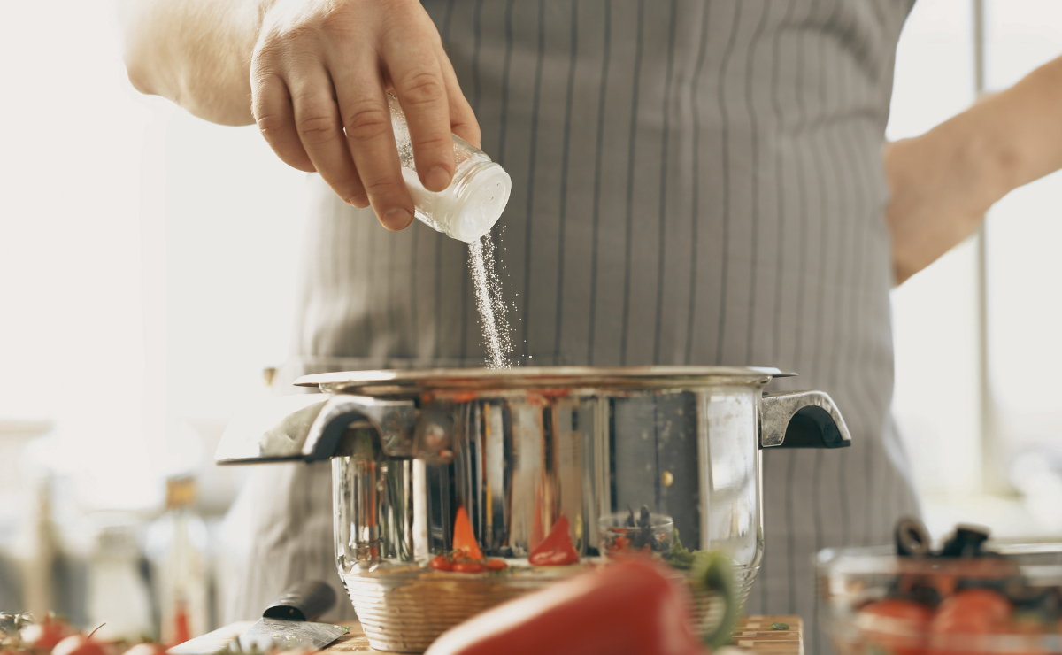 Pessoa adicionando sal em panela durante preparo de receita na cozinha.