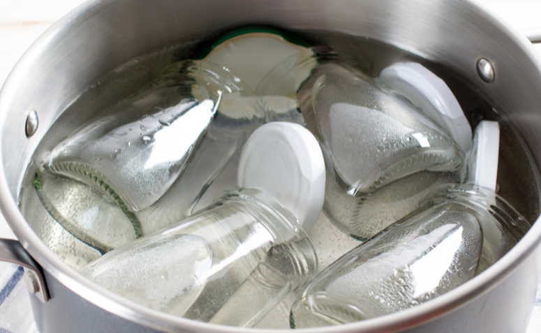 Potes de vidro sendo esterilizados em uma panela com água fervente antes de armazenar alimentos.