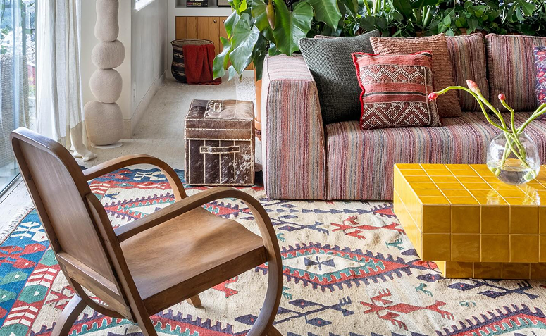 Sala de estilo boho com sofá estampado, tapete étnico, móveis de madeira e plantas na decoração.