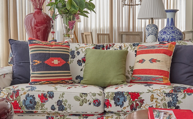 Sofá estampado floral com almofadas em tons de verde, azul e vermelho coordenadas com a decoração da sala.
