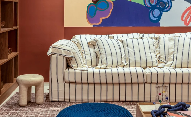 Sofá listrado em tons neutros combinado com parede terracota e quadro colorido na sala de estar.