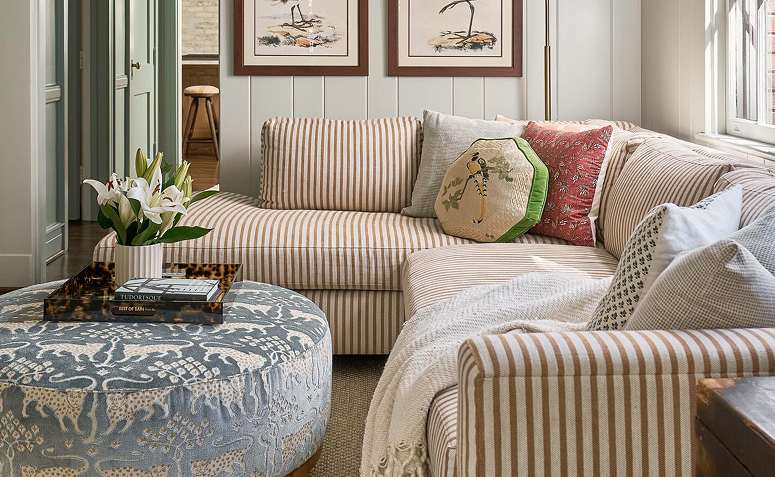 Sofá estampado listrado com almofadas de diferentes cores, estampas e texturas em sala de estar aconchegante.