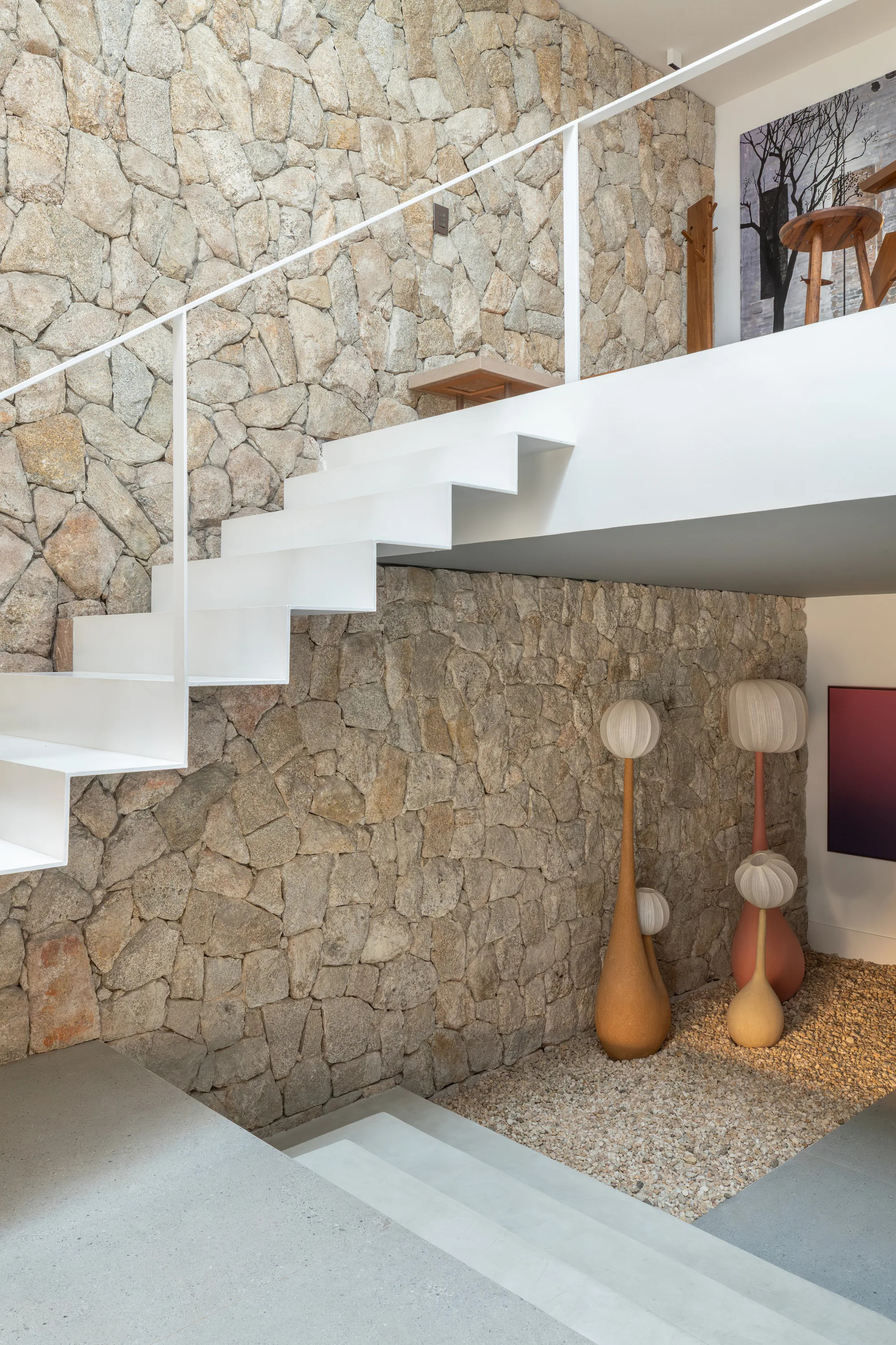 Hall de entrada com escada em aço branco, pedra moledo, pé-direito duplo e obras de arte contemporânea.