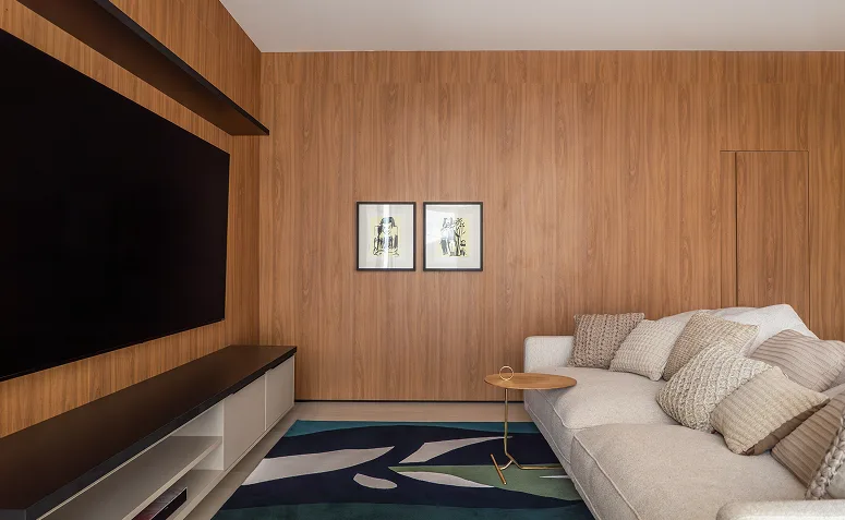 Sala de TV com tela grande instalada em painel de madeira, sofá próximo e rack baixo, destacando a relação entre tamanho da TV e conforto visual.