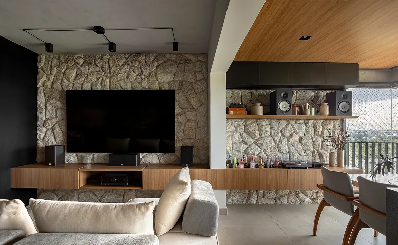 Ambiente integrado com TV na parede, sofá, área gourmet e sistema de som, mostrando como o uso do espaço influencia a escolha da tela.