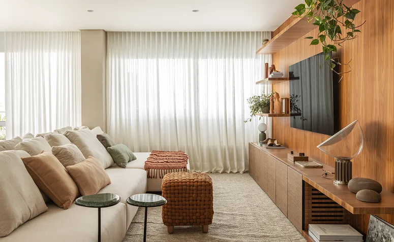 Sala iluminada com TV em painel de madeira, cortinas claras e sofá amplo, mostrando como luz natural e posicionamento influenciam a visualização.