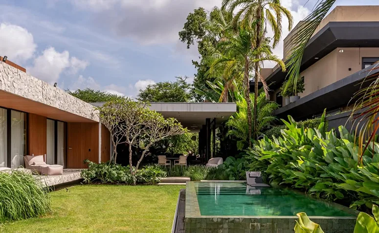 Piscina verde integrada ao jardim, com paisagismo tropical e área externa de casa contemporânea.