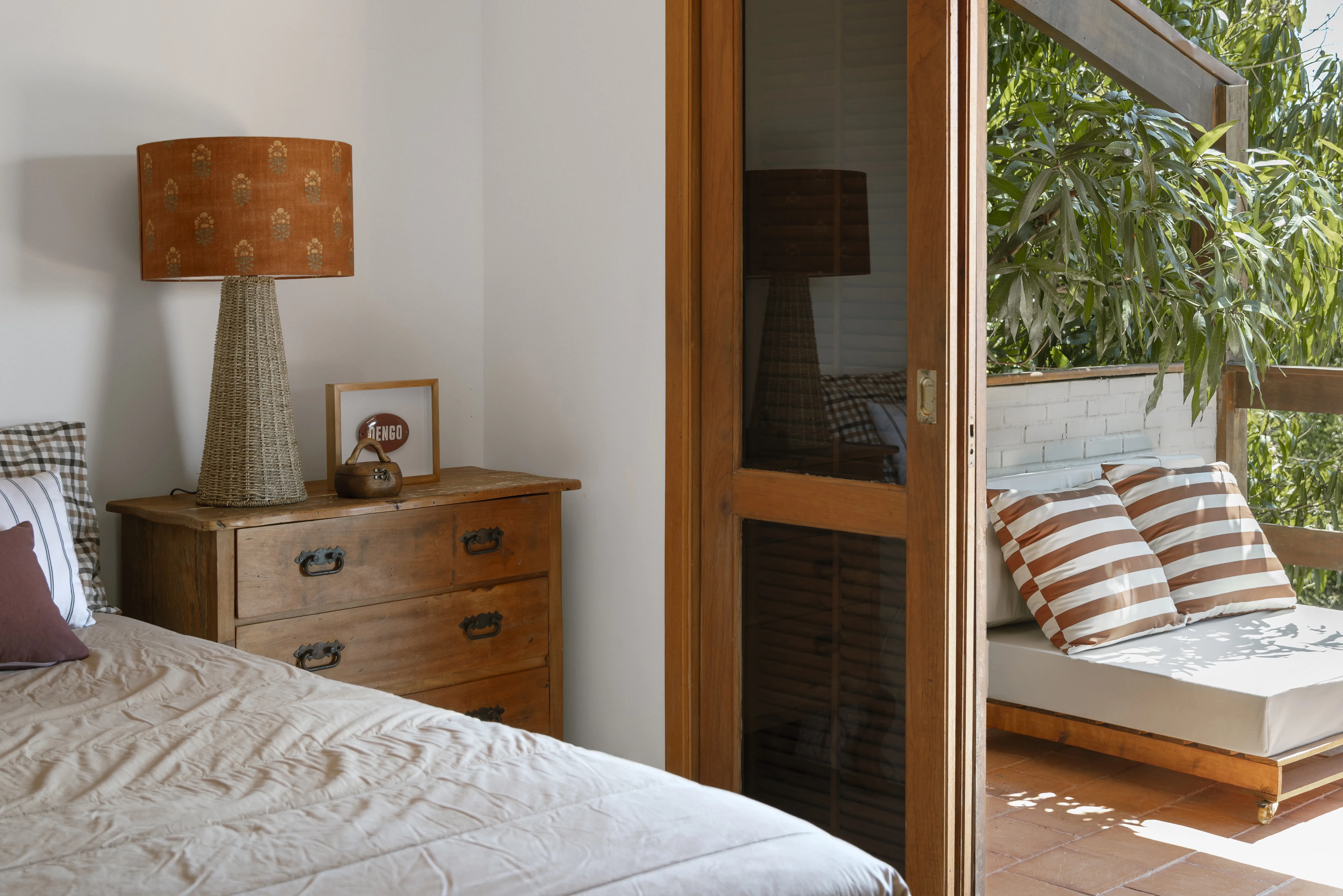 Quarto aconchegante com esquadrias de madeira, tecidos estampados e decoração em tons naturais.