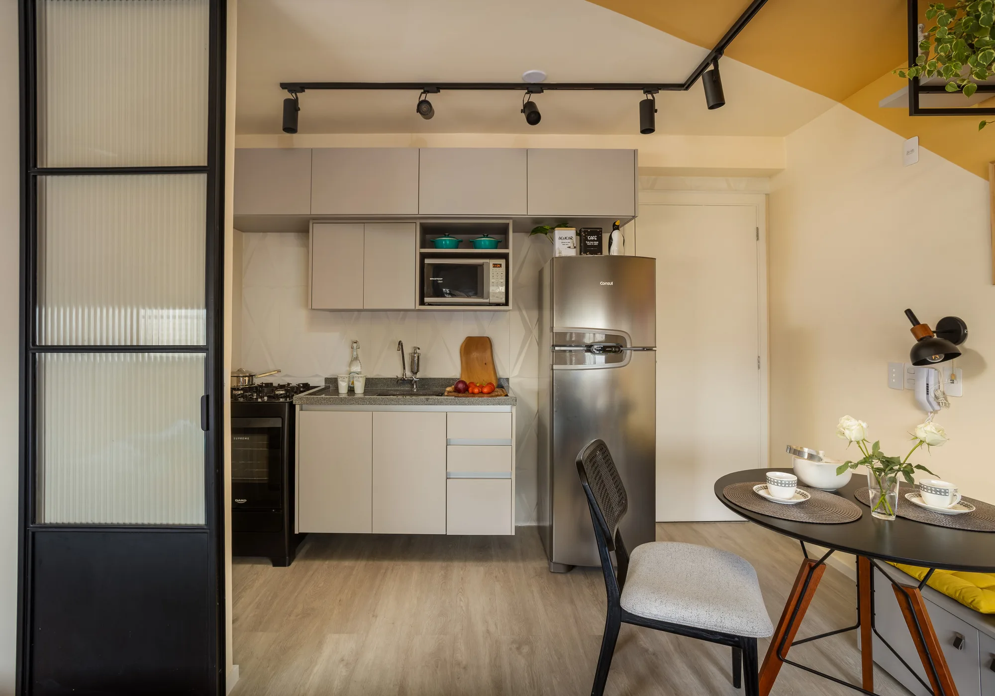 Cozinha compacta com armários cinza, nicho para micro-ondas, bancada clara e revestimento cerâmico com relevo na área molhada.