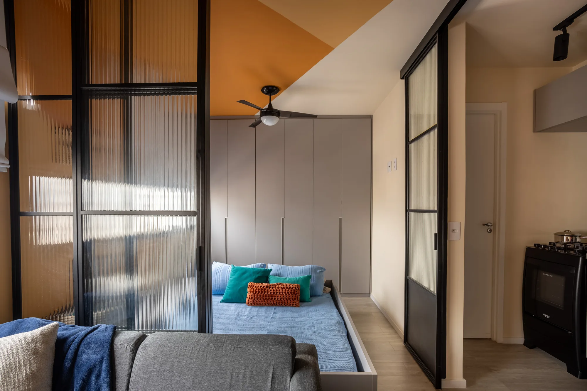 Quarto compacto com cama baixa em marcenaria cinza, pintura geométrica nas paredes e guarda-roupa planejado.