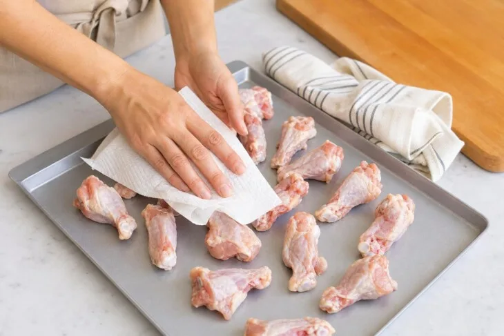 Mãos secando pedaços de frango a passarinho com papel-toalha antes de fritar.