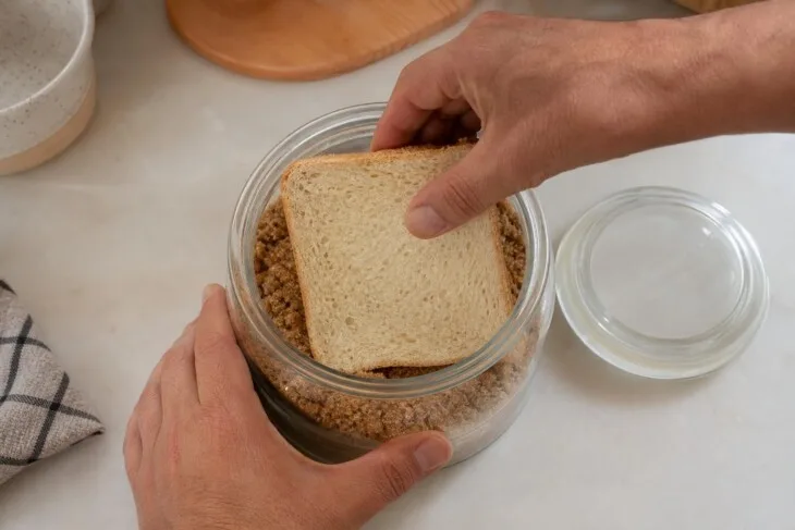 Fatia de pão colocada sobre açúcar mascavo endurecido dentro de um pote de vidro.