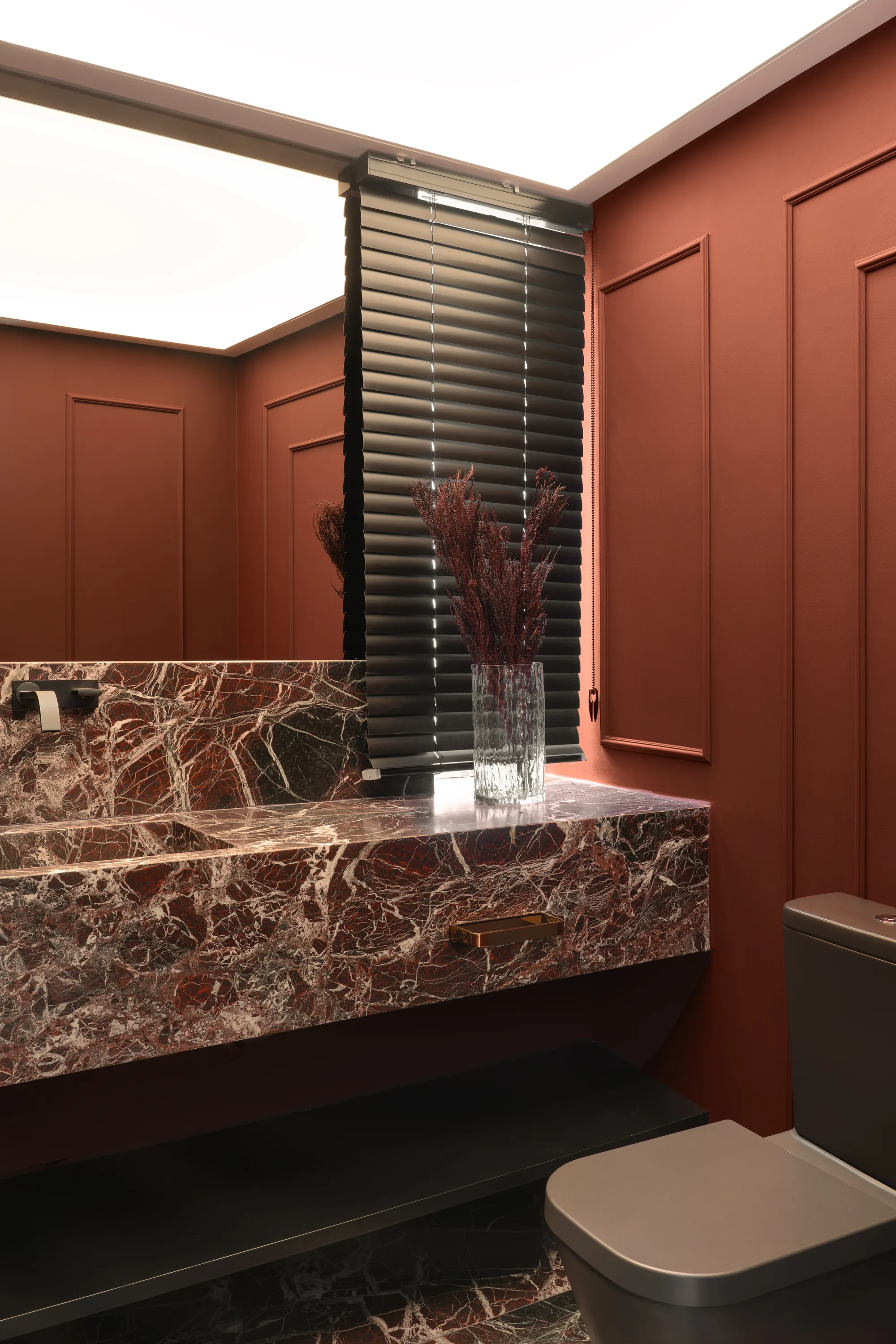 Lavabo em tons de vinho com boiseries e bancada com cuba esculpida em mármore vermelho.