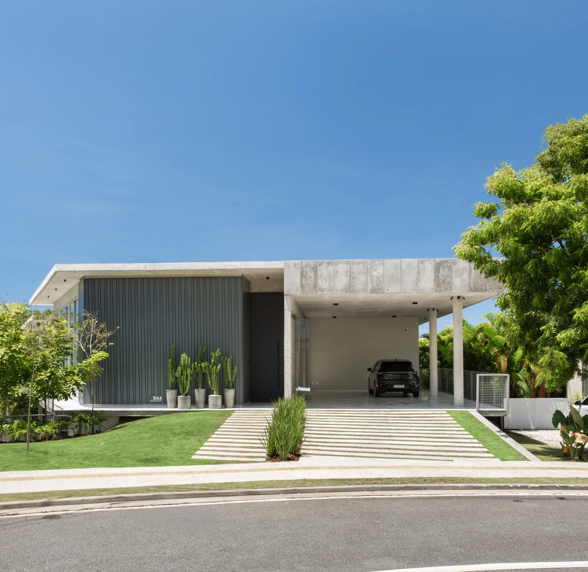 Fachada de casa brutalista com concreto aparente, linhas retas e paisagismo.