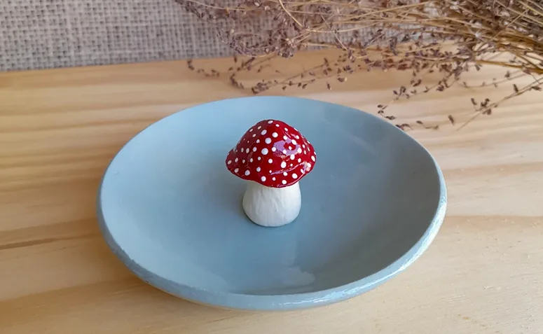 pratinho decorativo de cerâmica fria azul com pequeno cogumelo vermelho.