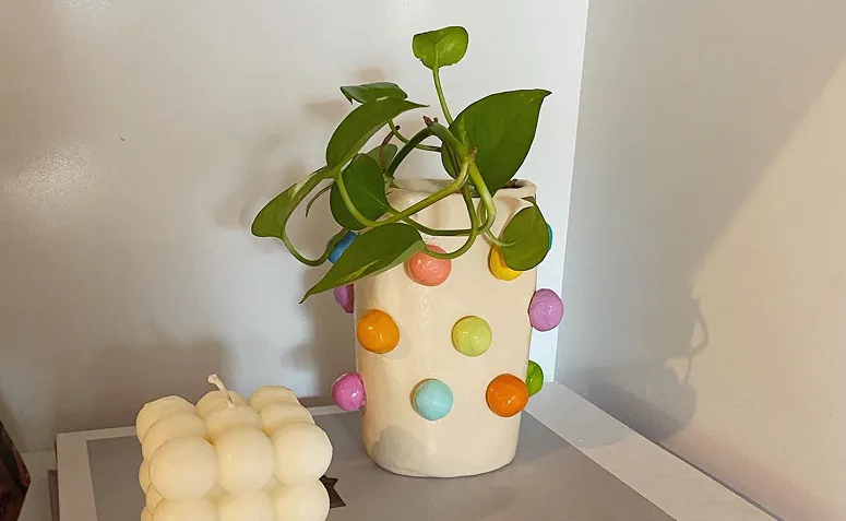 cachepô decorativo de cerâmica fria com aplicações coloridas e planta verde.