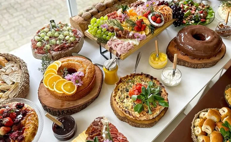 Mesa de brunch com bolos, quiche, frutas, frios, pães e diferentes acompanhamentos