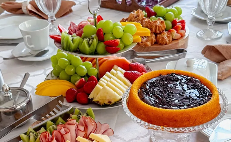 Frutas cortadas, bolo, frios e salgados organizados em travessas para servir no brunch
