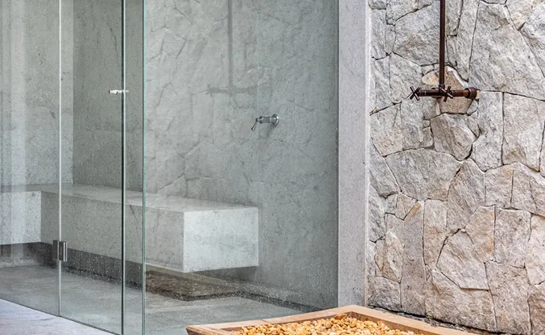 sauna a vapor com fechamento de vidro e revestimentos em pedra.