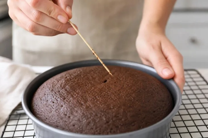 Palito com migalhas úmidas sendo retirado do centro de um bolo de chocolate.