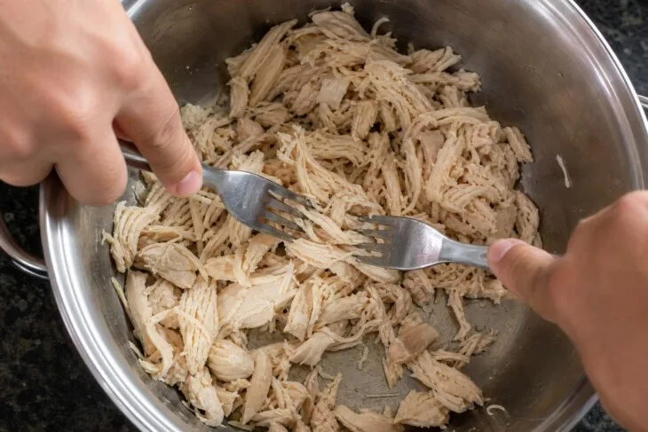 Dois garfos desfiando frango cozido dentro de uma panela.