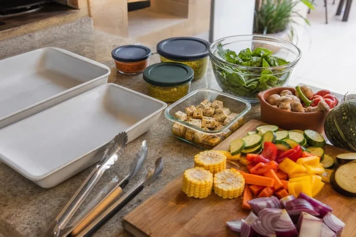 Bancada organizada com legumes, tofu, travessas e utensílios separados para churrasco vegetariano.