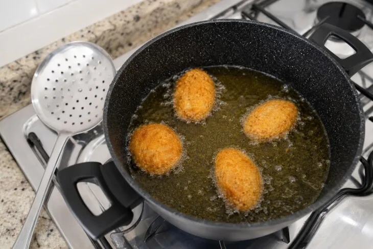 Bolinhos empanados fritando em óleo quente com espaço entre eles.