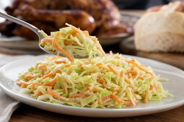 Colher servindo salada de repolho e cenoura com molho cremoso aderido aos vegetais.