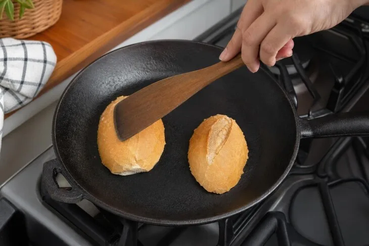 Duas metades de pão francês com o miolo voltado para baixo em uma frigideira.