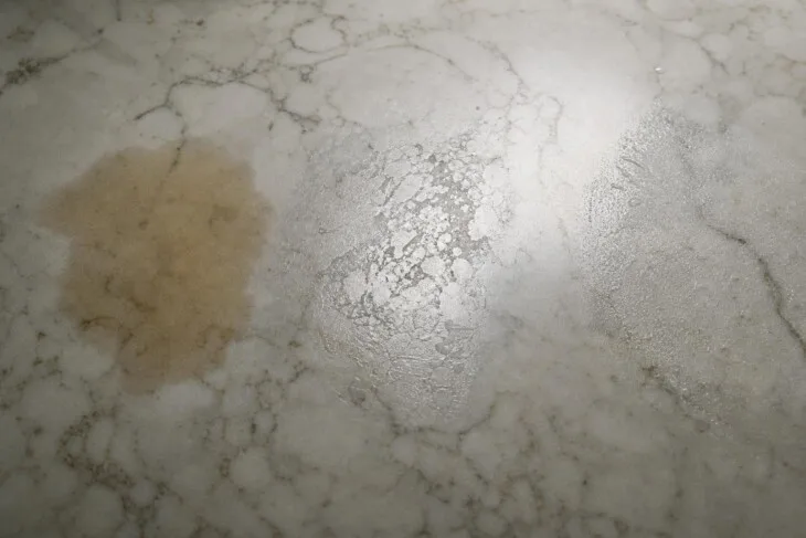 Detalhe de mármore com área escurecida, trecho fosco e resíduo superficial.