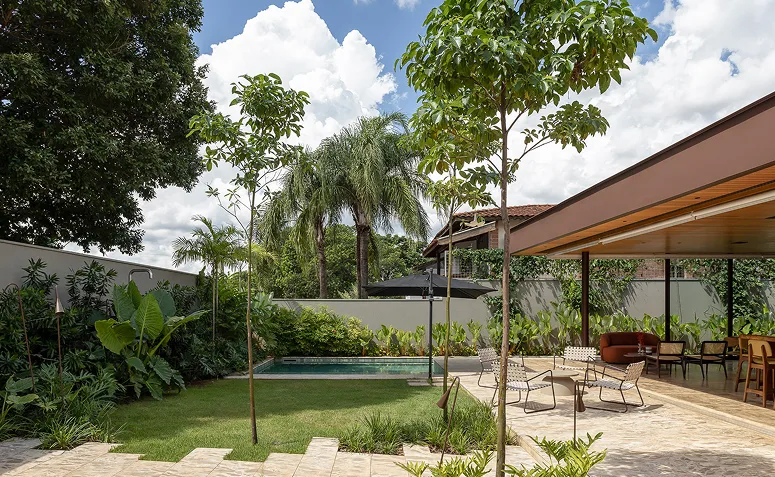 Jardim sensorial residencial com gramado, árvores, piscina e varanda integrada à vegetação.