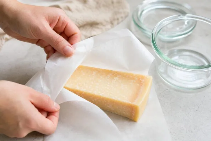 Pedaço de queijo duro sendo embrulhado em papel-manteiga antes de ir para um pote.