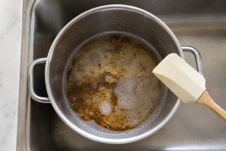 Crosta no fundo da panela de inox coberta por água com detergente para ficar de molho.